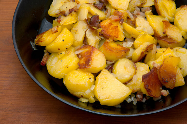 A skillet filled with golden brown roasted potatoes mixed with bits of bacon and onions.