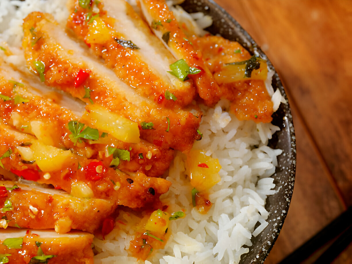 A close-up of sliced chicken topped with a fruity sauce and served over a bed of fluffy white rice.