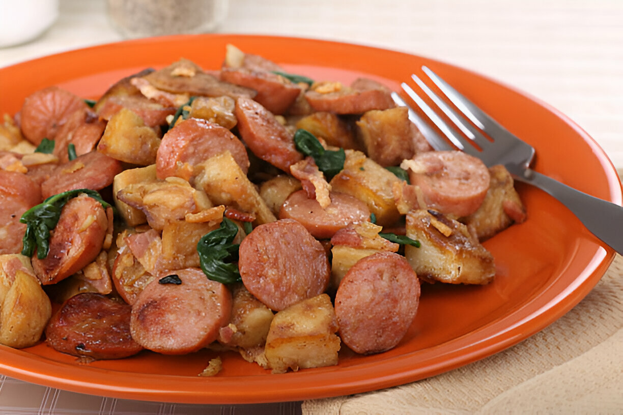 A colorful plate of cooked sausage, potatoes, and spinach garnished with crispy bits, served on an orange plate.