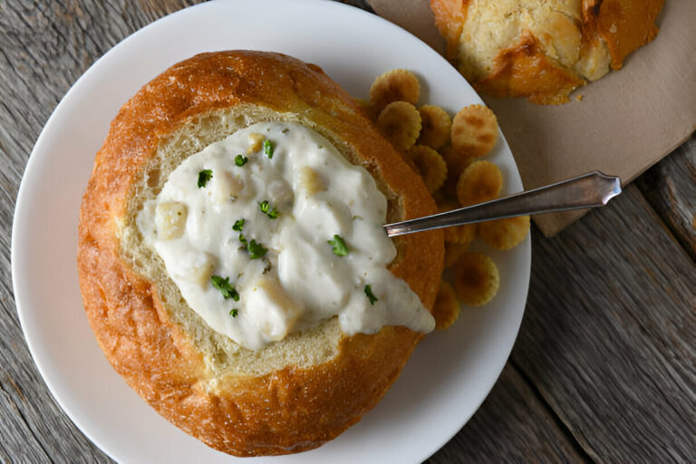 A hearty bowl of clam chowder served in a bread bowl with crackers on the side.