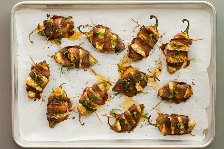 A platter of stuffed jalapeño peppers wrapped in bacon, garnished with fresh herbs.