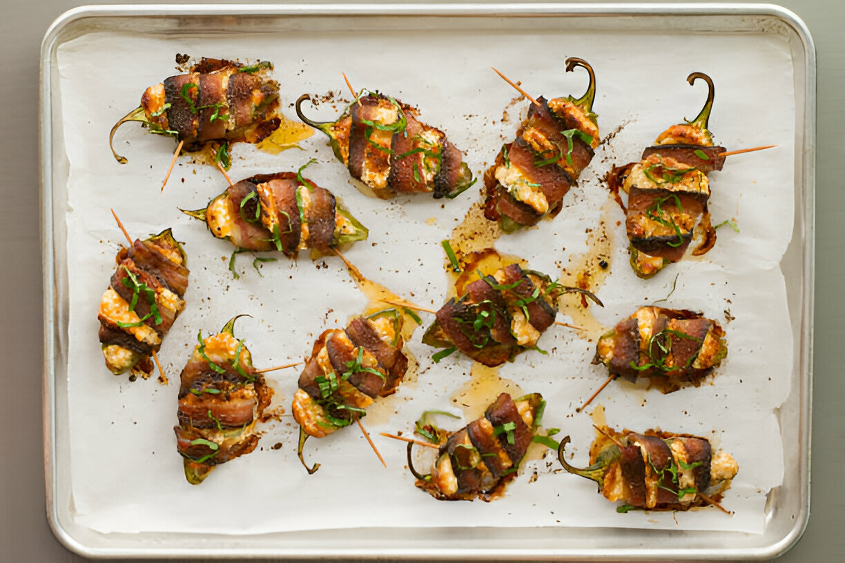 A platter of stuffed jalapeño peppers wrapped in bacon, garnished with fresh herbs.