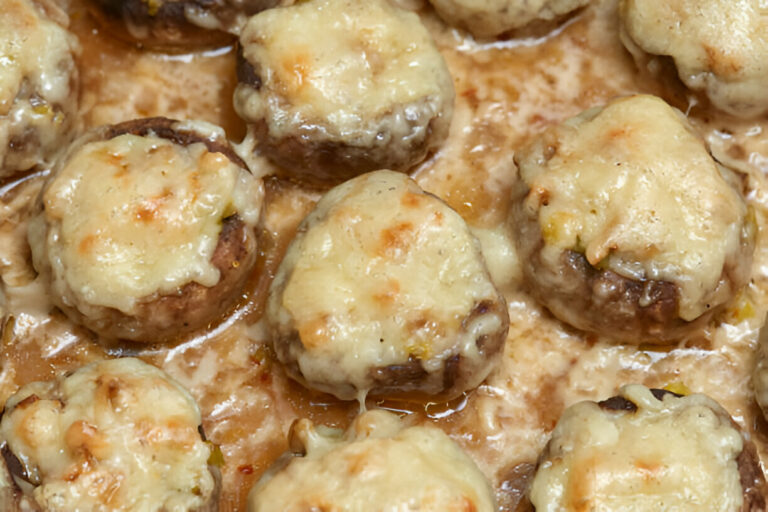 A close-up view of stuffed mushrooms topped with melted cheese in a baking dish.