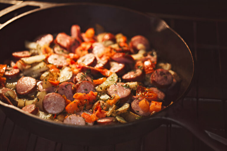 A close-up view of sautéed sausage and vegetables in a cast iron skillet.