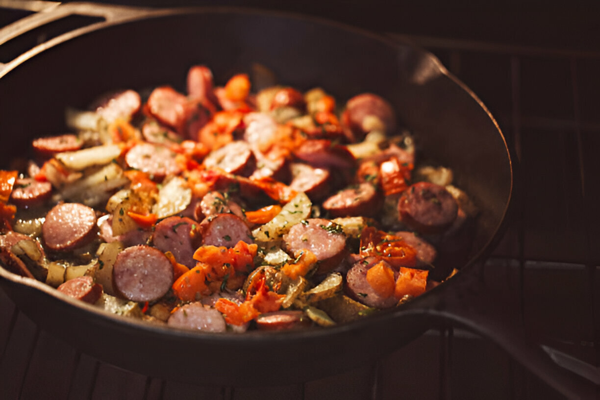 A close-up view of sautéed sausage and vegetables in a cast iron skillet.