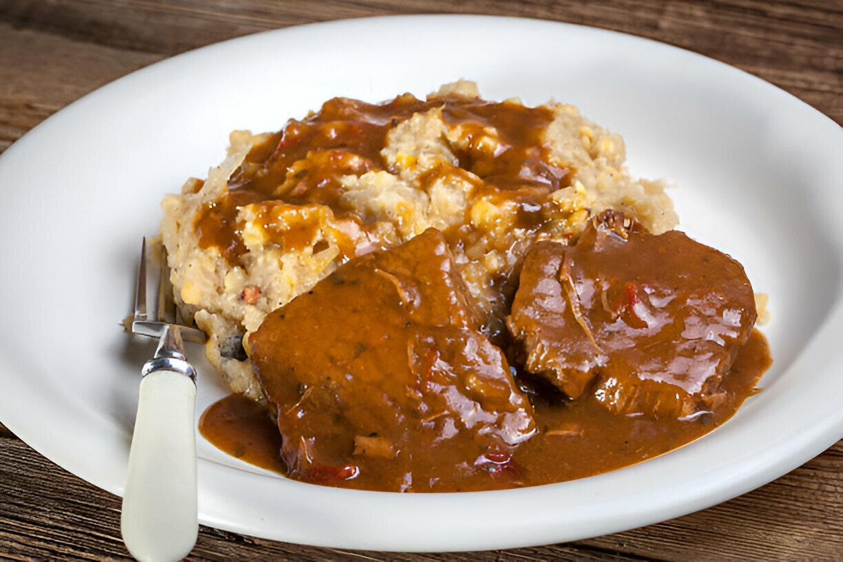 Plate of beef with gravy served over mashed potatoes