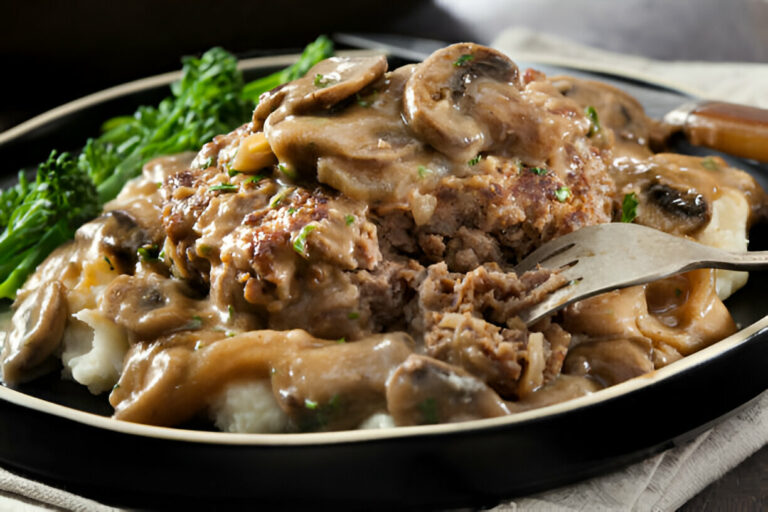 A plate of meatloaf topped with gravy and mushrooms served with mashed potatoes and broccolini.