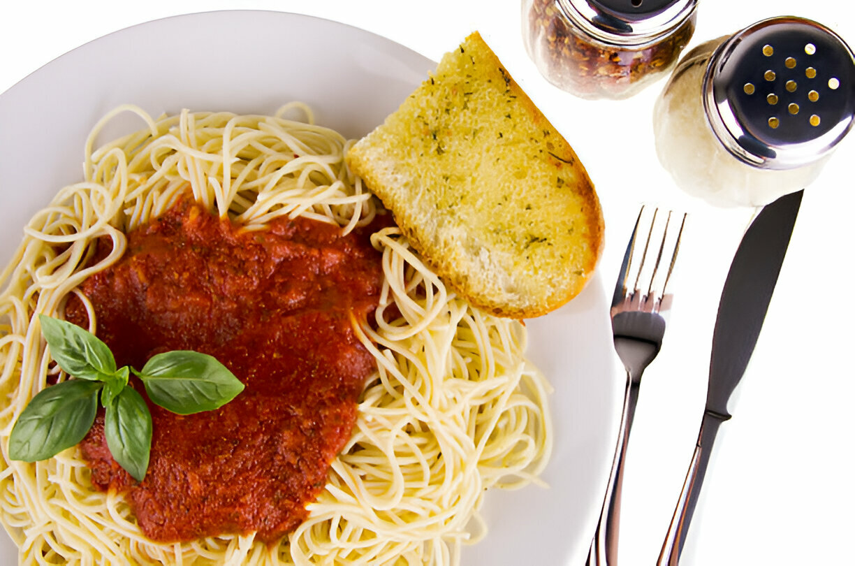 Plate of spaghetti with marinara sauce, a slice of garlic bread, and condiments including salt and pepper shakers.