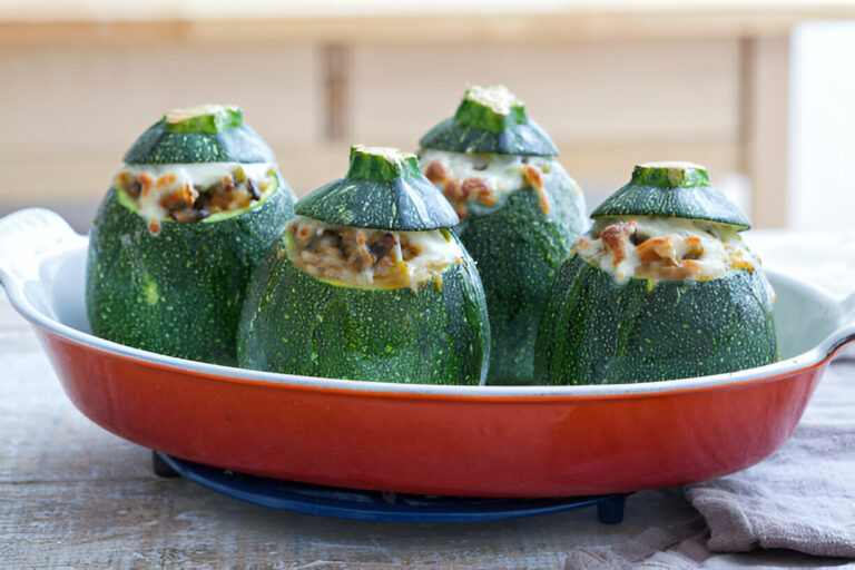 Four stuffed zucchini in a red baking dish with a light kitchen background.