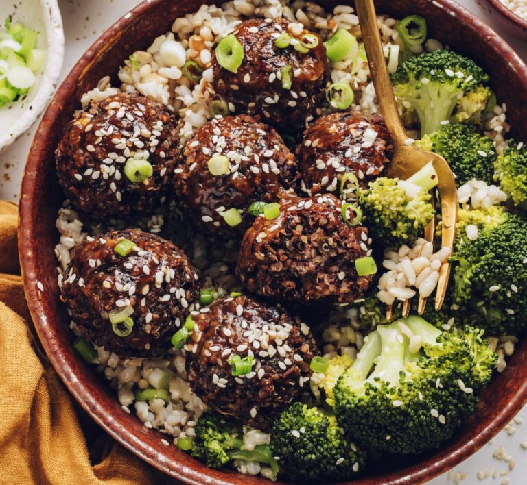 A bowl of meatballs with sesame seeds on top, served over brown rice and surrounded by broccoli florets.