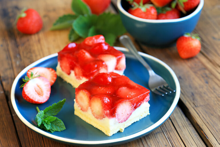 A close-up of two pieces of strawberry dessert on a blue plate, garnished with fresh strawberries and mint leaves.