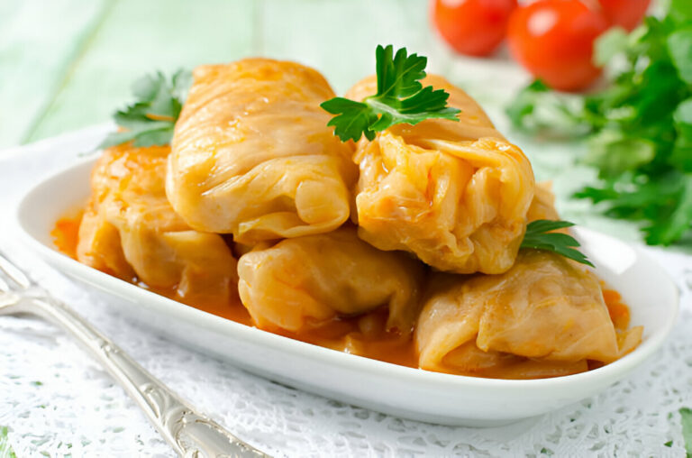 Delicious cabbage rolls served in a white dish with garnish on a light table.