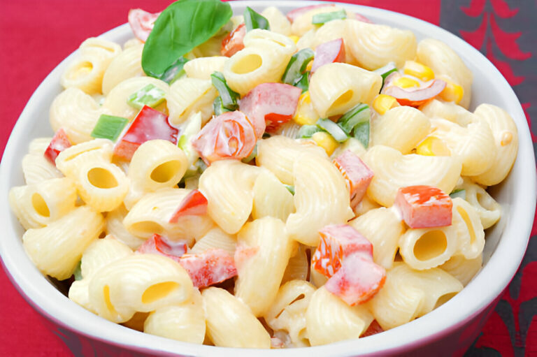 A bowl of creamy pasta salad with colorful vegetables including bell peppers and green onions.