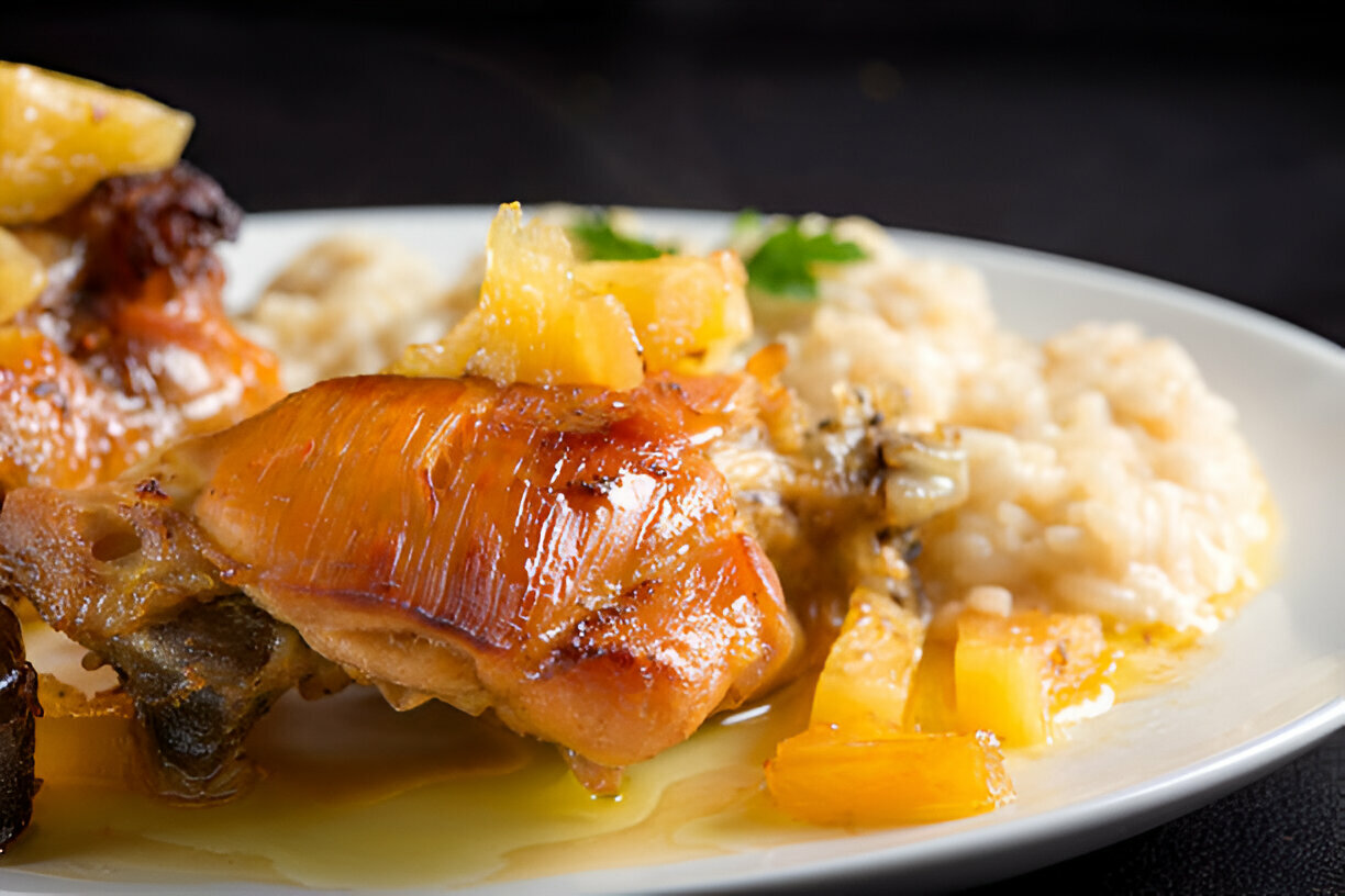 A close-up of a plate featuring tender chicken thigh topped with pineapple chunks and served alongside creamy rice.