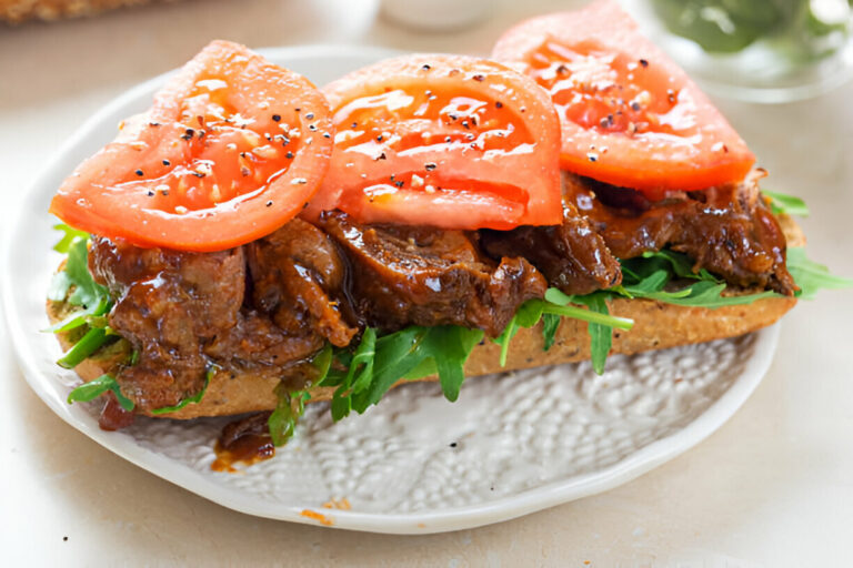 A delicious sandwich topped with fresh tomato slices, leafy greens, and juicy beef on a plate.