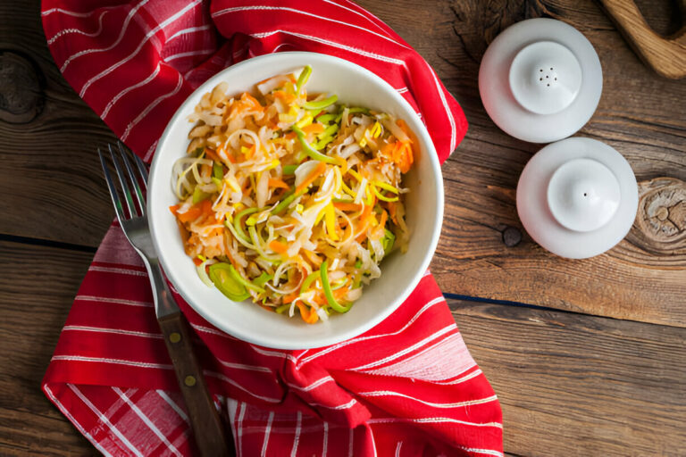 A bowl of colorful vegetable salad on a wooden table with salt and pepper shakers.