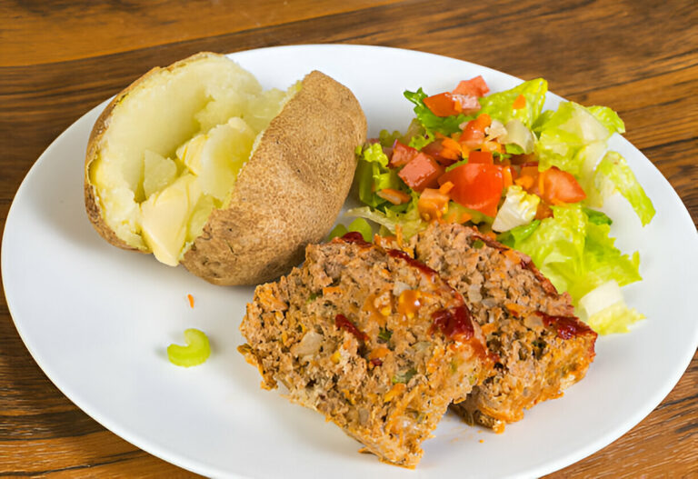 A plate featuring a baked potato with butter, a slice of meatloaf drizzled with ketchup, and a side salad with lettuce, tomatoes, and carrots.