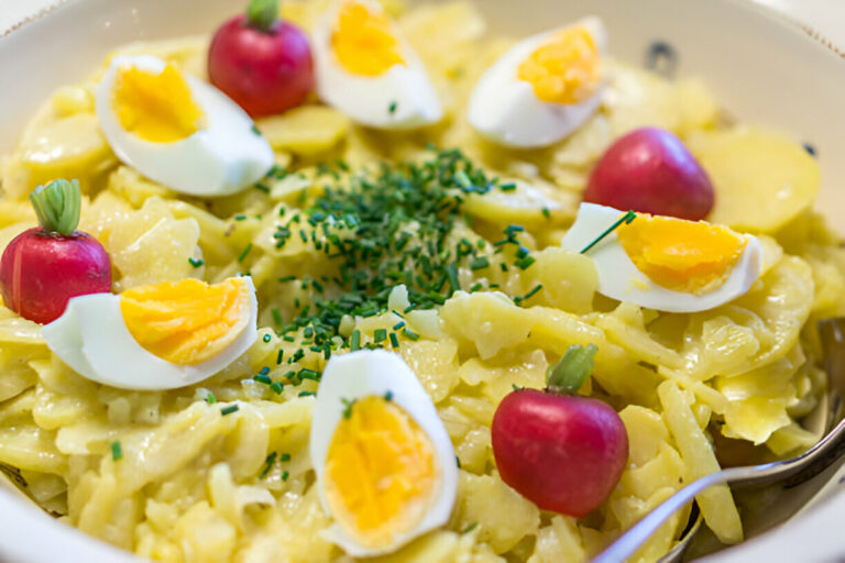 A bowl of creamy pasta topped with sliced boiled eggs and small red radishes, garnished with chopped chives.