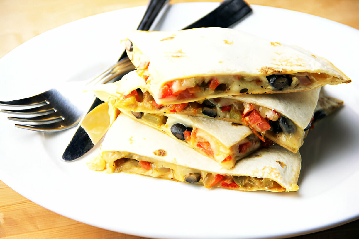 A plate of delicious quesadillas cut into triangles, filled with black beans, tomatoes, and cheese.