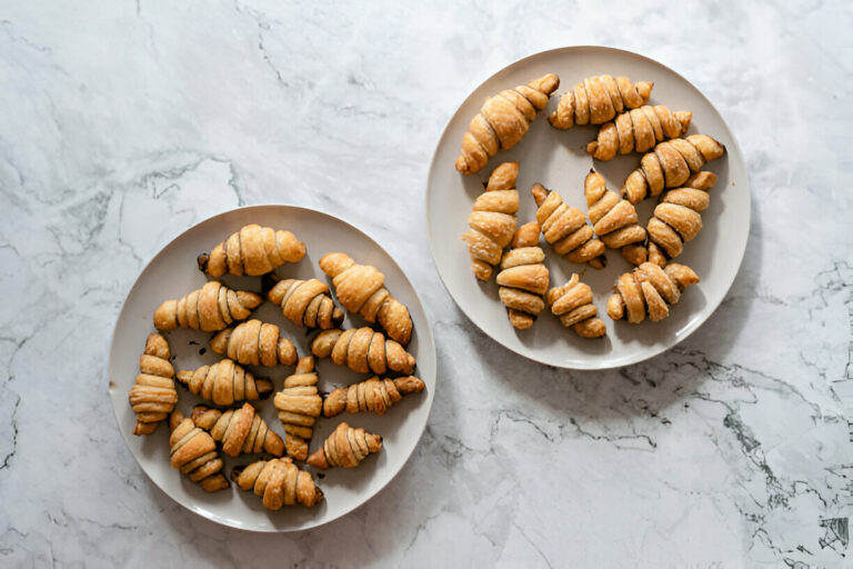 Two plates of freshly baked pastries shaped like croissants on a marble surface.