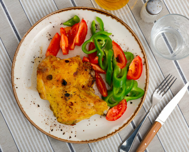 A plate of grilled chicken served with sliced tomatoes and green bell peppers on a wooden table.